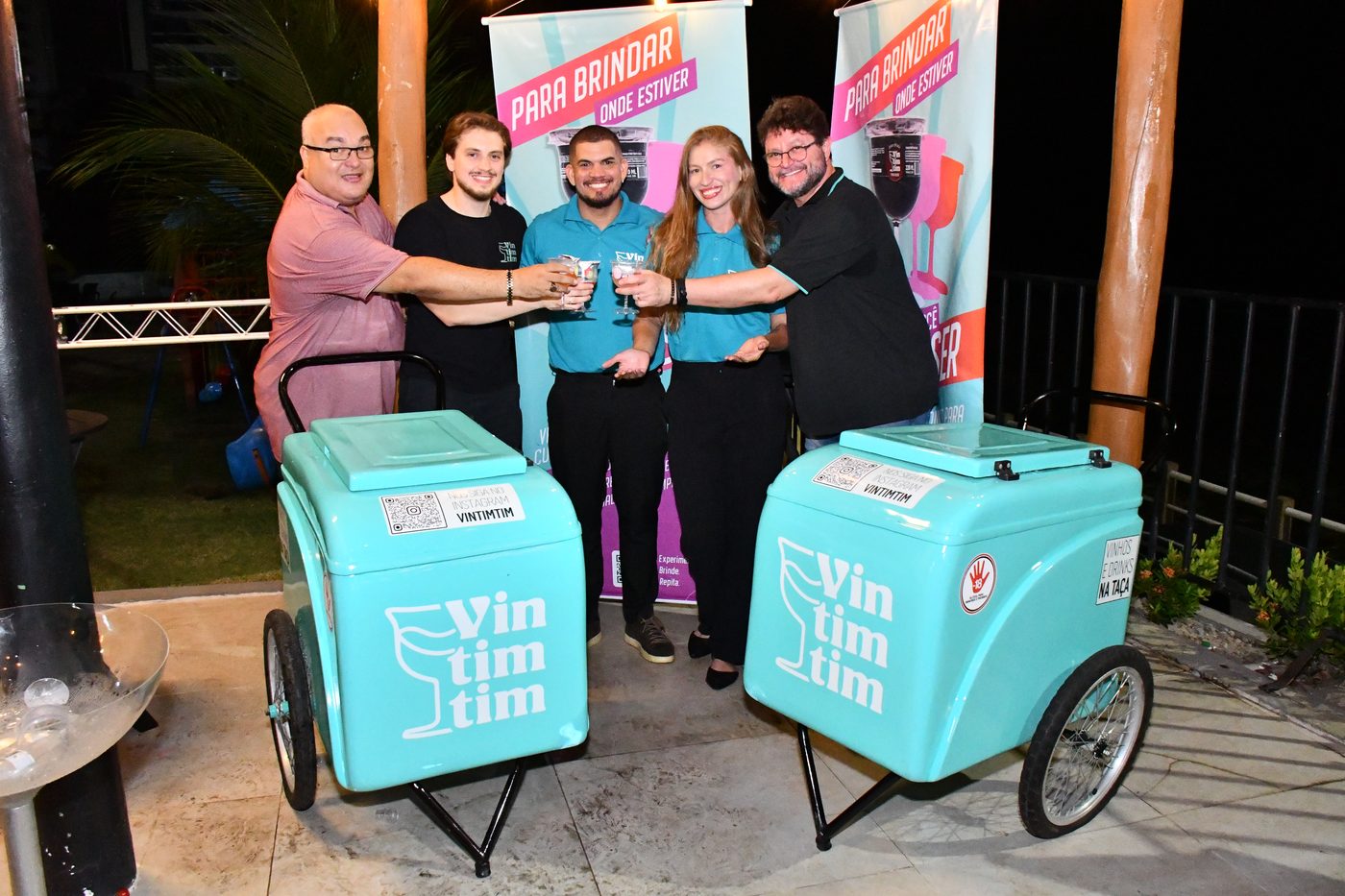 Equipe Vintimtim brindando entre dois carrinhos da marca, em evento noturno